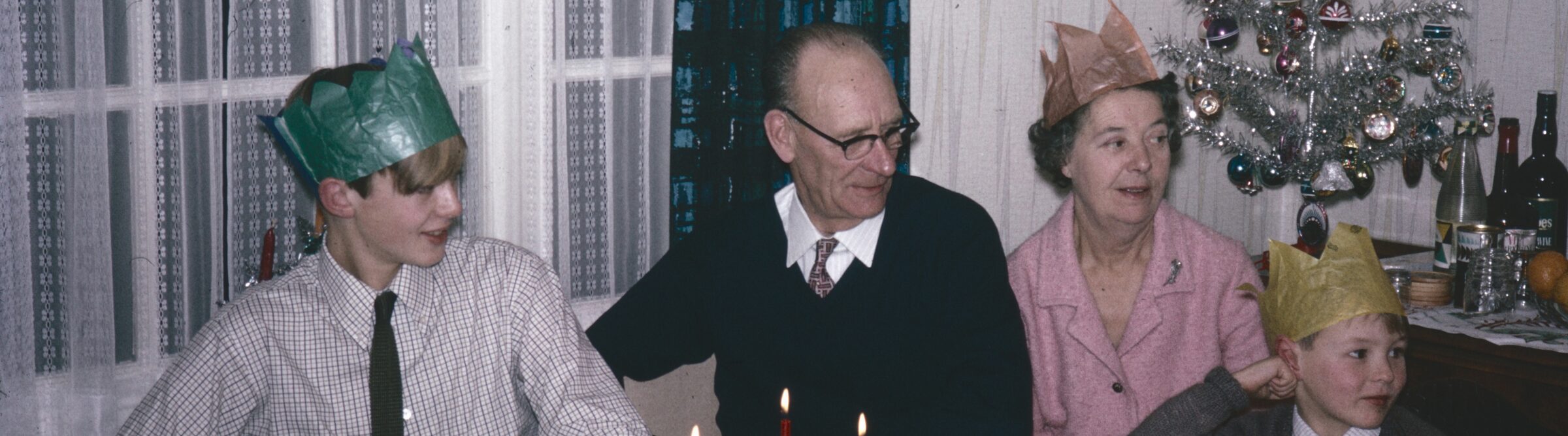 A family round the table at Christmas in the 1960s, paper hats on, mid-story